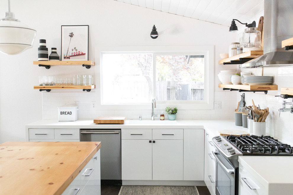 サクラメントにあるカントリー風のおしゃれなキッチン (一体型シンク、フラットパネル扉のキャビネット、白いキャビネット、白いキッチンパネル、サブウェイタイルのキッチンパネル、シルバーの調理設備、茶色い床、白いキッチンカウンター) の写真