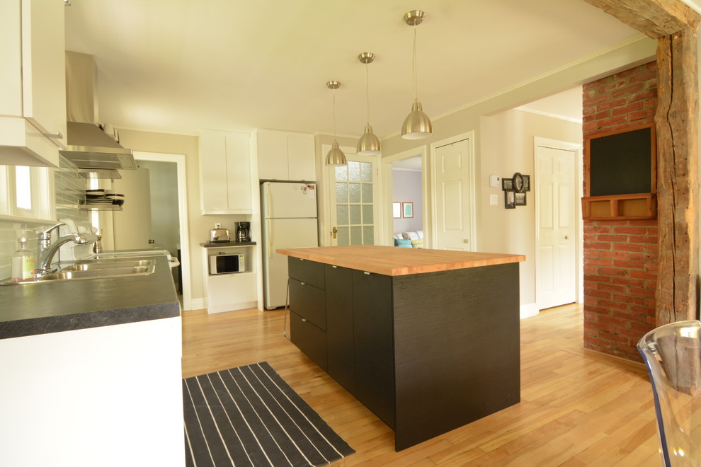 モントリオールにある低価格の小さなインダストリアルスタイルのおしゃれなキッチン (フラットパネル扉のキャビネット、木材カウンター、ガラスタイルのキッチンパネル、淡色無垢フローリング) の写真