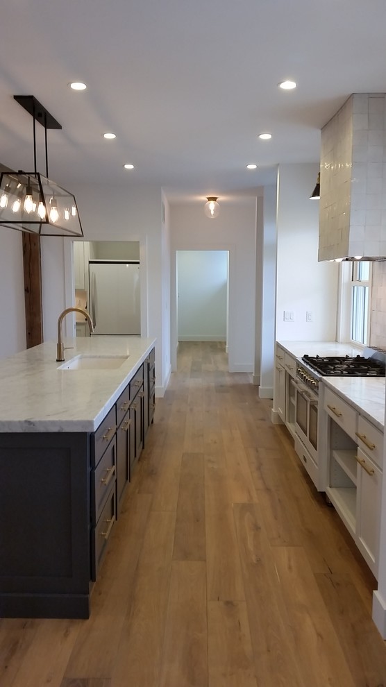 Cette image montre une cuisine ouverte linéaire rustique de taille moyenne avec des portes de placard blanches, une crédence beige, un électroménager en acier inoxydable, un sol en bois brun et îlot.