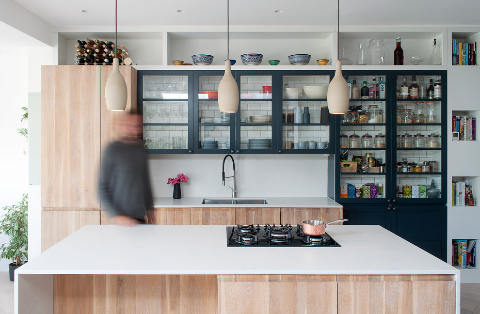 Cette photo montre une cuisine parallèle tendance en bois clair avec un évier encastré, un placard à porte vitrée, une crédence blanche, îlot, un sol beige et un plan de travail blanc.