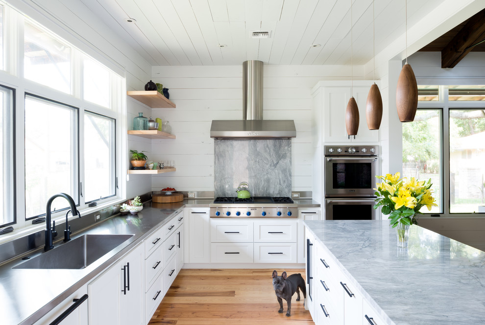 Exempel på ett klassiskt l-kök, med en integrerad diskho, skåp i shakerstil, vita skåp, bänkskiva i rostfritt stål, grått stänkskydd, rostfria vitvaror, mellanmörkt trägolv, en köksö och stänkskydd i marmor