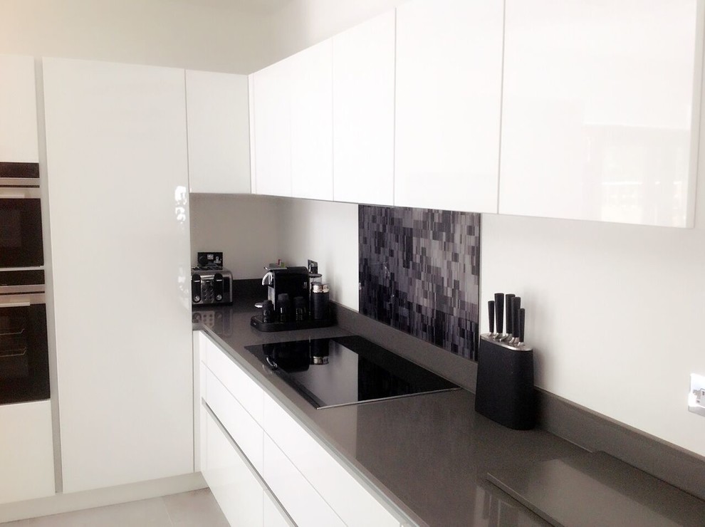 Foto på ett funkis u-kök, med en integrerad diskho, släta luckor, vita skåp, bänkskiva i kvartsit, flerfärgad stänkskydd, glaspanel som stänkskydd, integrerade vitvaror, klinkergolv i porslin och en köksö