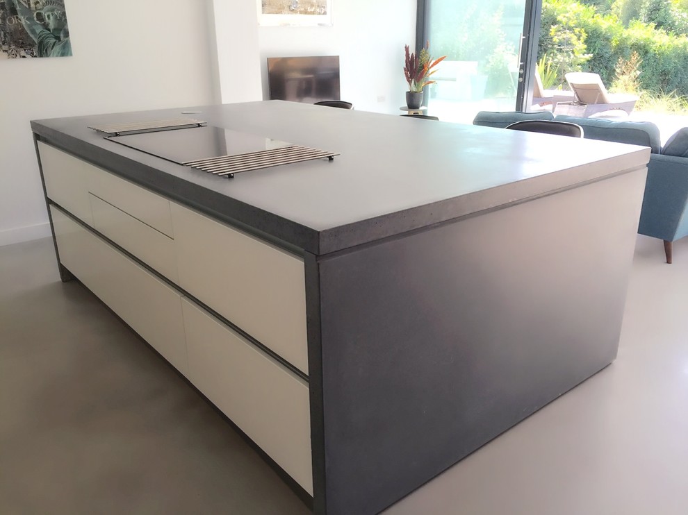 Inspiration for a contemporary open plan kitchen in Surrey with an integrated sink, white cabinets, concrete worktops, blue splashback, glass sheet splashback, concrete flooring, an island and integrated appliances.