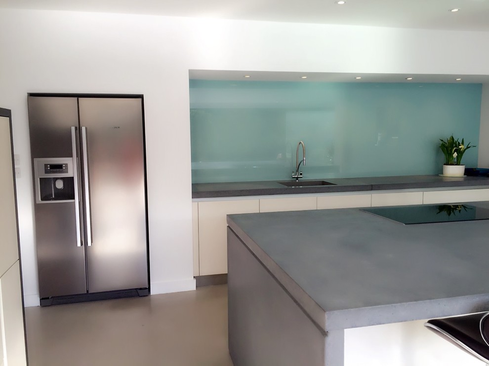 Photo of a contemporary open plan kitchen in Surrey with a built-in sink, white cabinets, concrete worktops, blue splashback, glass sheet splashback, integrated appliances, concrete flooring and an island.