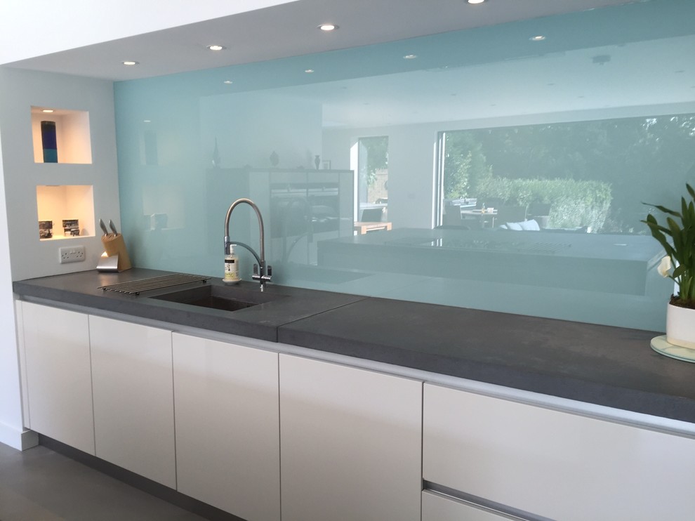 Design ideas for a contemporary open plan kitchen in Surrey with a built-in sink, concrete worktops, blue splashback, glass sheet splashback, integrated appliances, concrete flooring, white cabinets and an island.