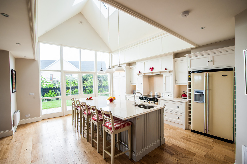 This is an example of a medium sized traditional single-wall kitchen/diner in Other with recessed-panel cabinets, beige cabinets, granite worktops, coloured appliances, medium hardwood flooring, an island, a built-in sink, beige splashback and stone slab splashback.