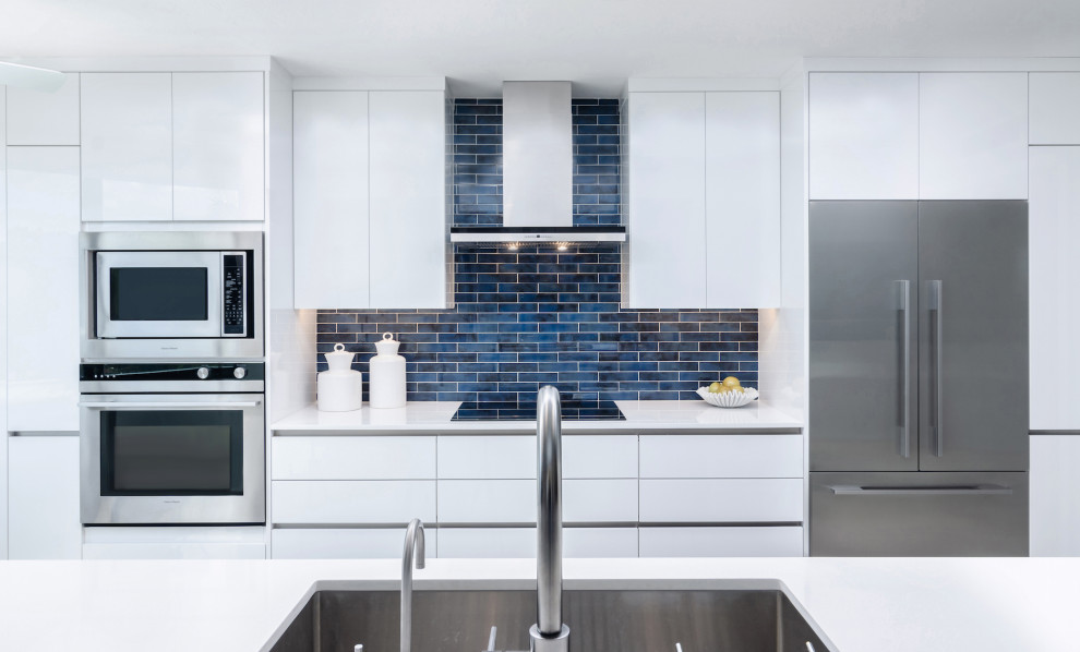 Zweizeilige Moderne Küche mit Unterbauwaschbecken, flächenbündigen Schrankfronten, weißen Schränken, Küchenrückwand in Blau, Küchengeräten aus Edelstahl, Kücheninsel und weißer Arbeitsplatte in Sonstige