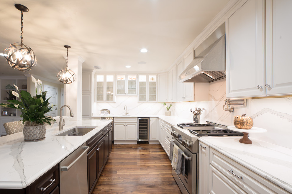 This is an example of a large classic l-shaped open plan kitchen in Atlanta with a submerged sink, raised-panel cabinets, white cabinets, marble worktops, white splashback, stone slab splashback, stainless steel appliances, dark hardwood flooring, an island, brown floors and white worktops.