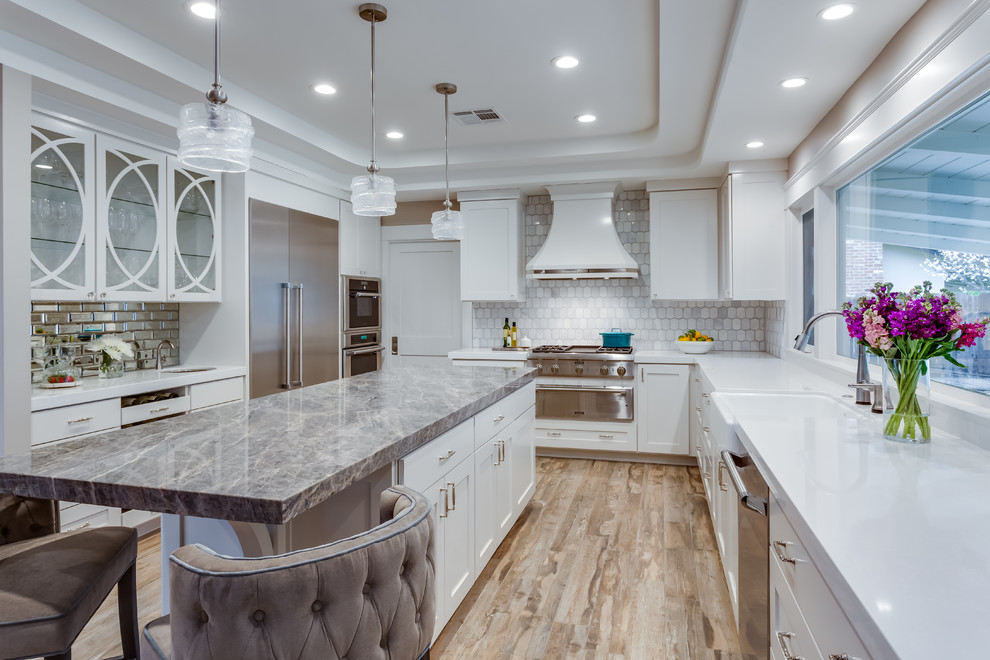 This is an example of a large traditional u-shaped enclosed kitchen in Sacramento with a belfast sink, shaker cabinets, white cabinets, quartz worktops, grey splashback, marble splashback, stainless steel appliances, an island, brown floors, white worktops and porcelain flooring.