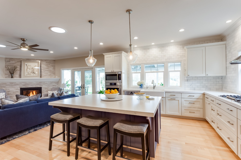 This is an example of a large classic l-shaped open plan kitchen in Sacramento with a belfast sink, recessed-panel cabinets, white cabinets, quartz worktops, white splashback, metro tiled splashback, stainless steel appliances, light hardwood flooring, an island, beige floors and white worktops.
