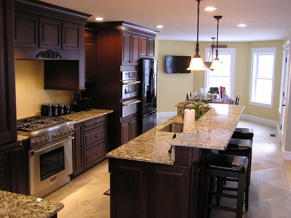 Exempel på ett klassiskt l-kök, med en undermonterad diskho, luckor med upphöjd panel, skåp i mörkt trä, granitbänkskiva, klinkergolv i porslin och en köksö