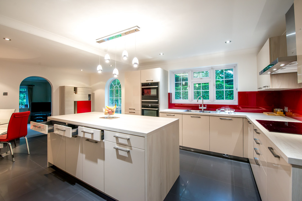 Kitchen - contemporary l-shaped kitchen idea in London with a double-bowl sink, flat-panel cabinets, light wood cabinets, onyx countertops, red backsplash, glass sheet backsplash, black appliances and an island