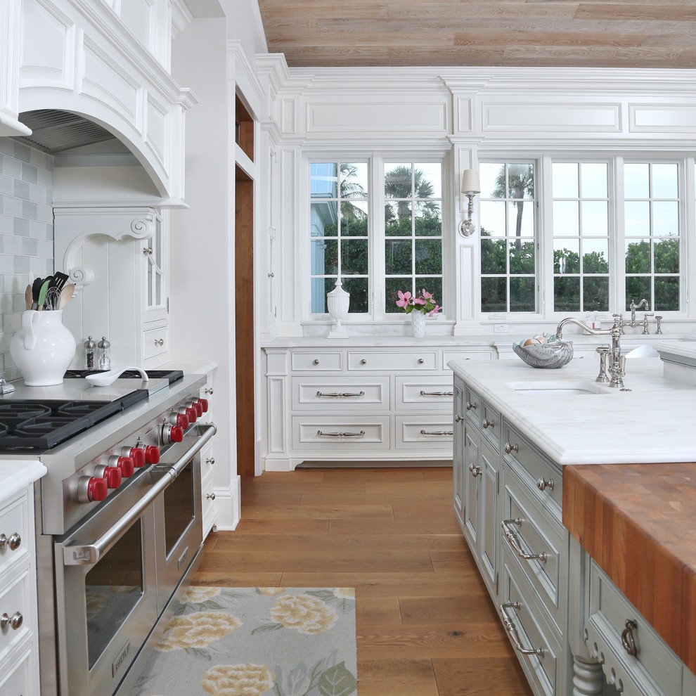 Example of a large classic l-shaped medium tone wood floor open concept kitchen design in Miami with a farmhouse sink, beaded inset cabinets, white cabinets, marble countertops, glass tile backsplash, paneled appliances and an island