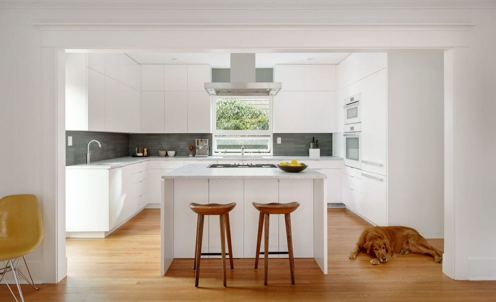 Immagine di un cucina con isola centrale minimal con ante lisce, ante bianche, top in marmo, elettrodomestici in acciaio inossidabile e parquet chiaro