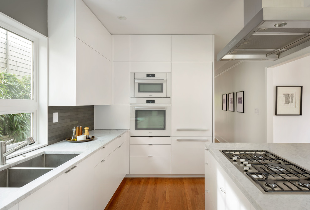 Idee per una cucina moderna con ante lisce, ante bianche, top in marmo, elettrodomestici in acciaio inossidabile e parquet chiaro