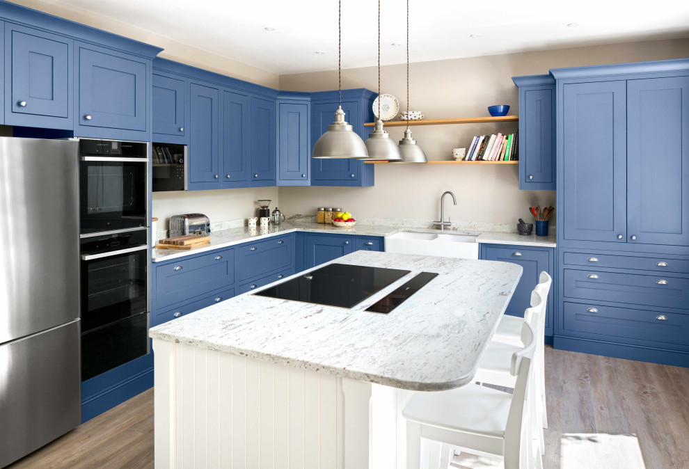 Large beach style l-shaped kitchen/diner in Other with a belfast sink, shaker cabinets, blue cabinets, granite worktops, granite splashback, black appliances and an island.