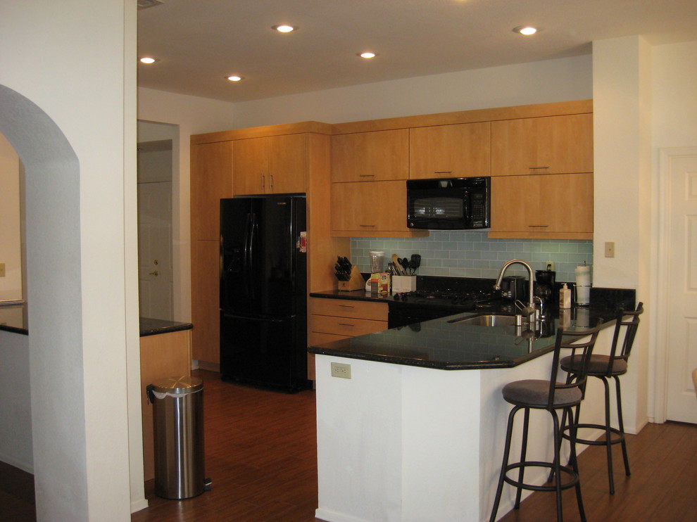 Example of a minimalist u-shaped enclosed kitchen design in Las Vegas with an undermount sink, flat-panel cabinets, light wood cabinets, granite countertops, glass tile backsplash and black appliances
