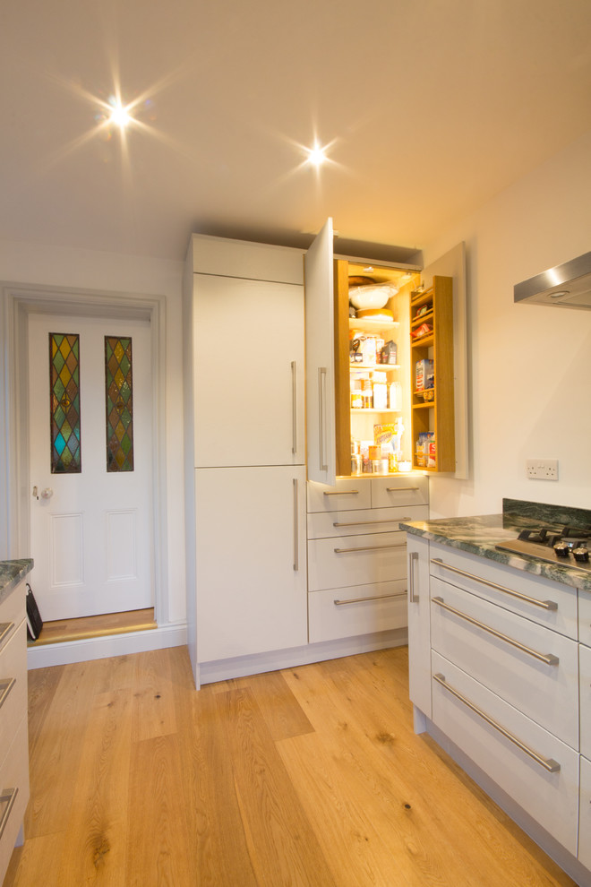 Example of a mid-sized minimalist u-shaped medium tone wood floor enclosed kitchen design in London with a drop-in sink, flat-panel cabinets, gray cabinets, granite countertops, green backsplash, stone slab backsplash, paneled appliances and no island
