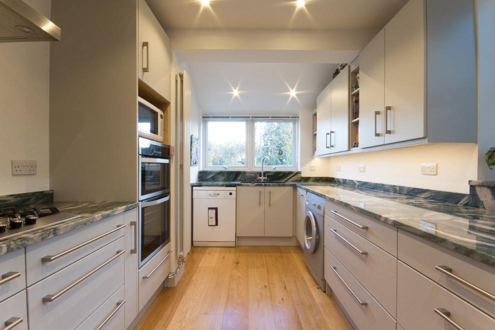 This is an example of a medium sized modern grey and cream u-shaped enclosed kitchen in London with a built-in sink, flat-panel cabinets, grey cabinets, granite worktops, green splashback, stone slab splashback, integrated appliances, medium hardwood flooring and no island.