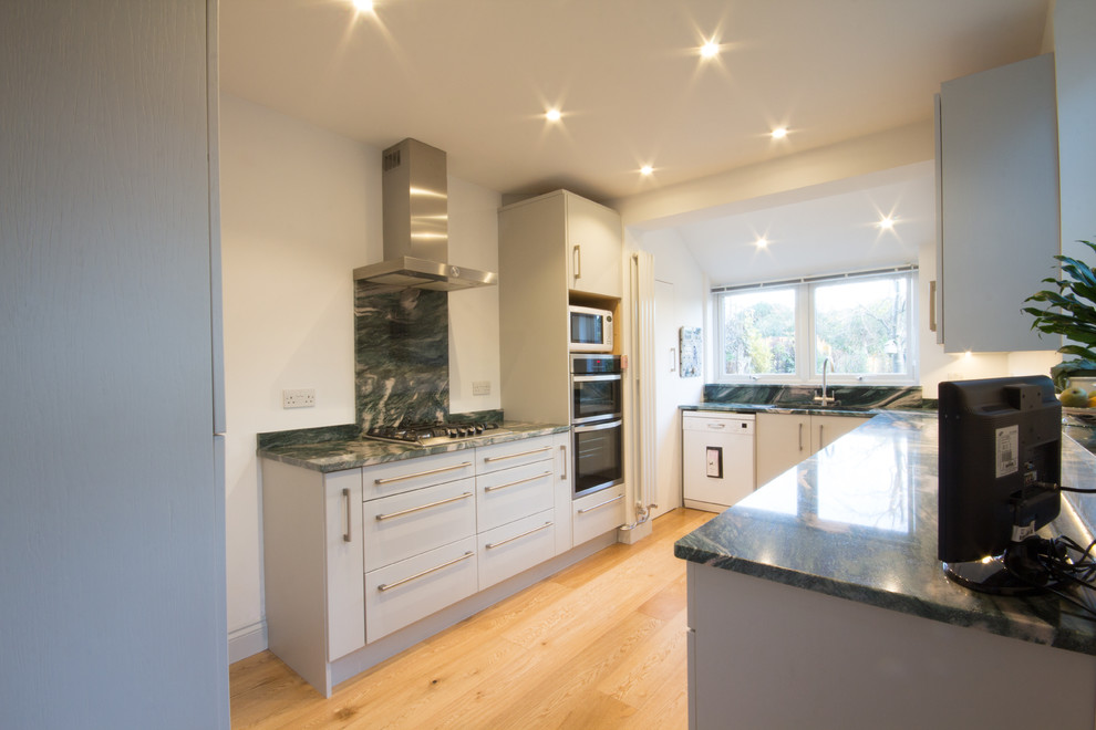 This is an example of a medium sized modern u-shaped enclosed kitchen in London with a built-in sink, flat-panel cabinets, grey cabinets, granite worktops, green splashback, stone slab splashback, integrated appliances, medium hardwood flooring and no island.