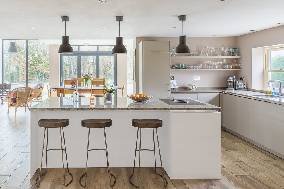 Foto på ett stort funkis kök med öppen planlösning, med en undermonterad diskho, släta luckor, vita skåp, granitbänkskiva, ljust trägolv, en köksö och brunt golv
