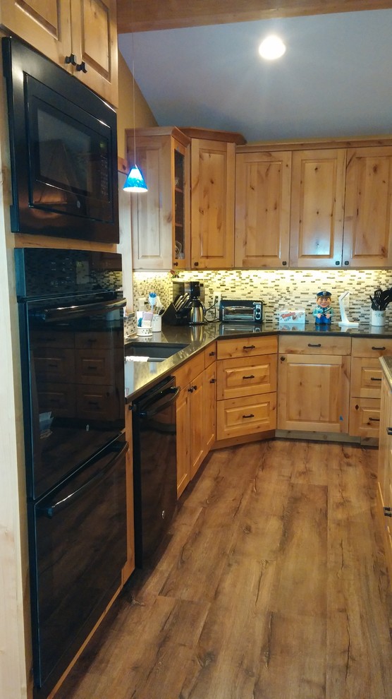 Rustik inredning av ett mellanstort kök, med en dubbel diskho, granitbänkskiva, grått stänkskydd, stänkskydd i glaskakel, svarta vitvaror, mellanmörkt trägolv, en köksö och brunt golv