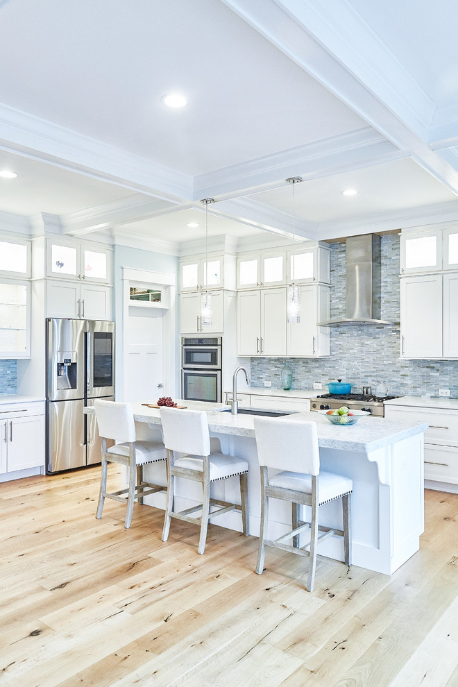 Klassisk inredning av ett stort vit vitt kök, med en undermonterad diskho, skåp i shakerstil, vita skåp, blått stänkskydd, stänkskydd i stickkakel, rostfria vitvaror, ljust trägolv, en köksö och beiget golv