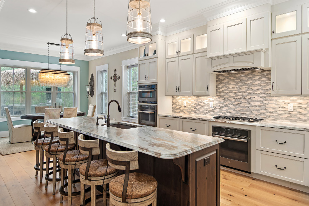 Example of a transitional galley medium tone wood floor and brown floor kitchen design in Other with an undermount sink, recessed-panel cabinets, gray cabinets, gray backsplash, mosaic tile backsplash, stainless steel appliances, an island and gray countertops