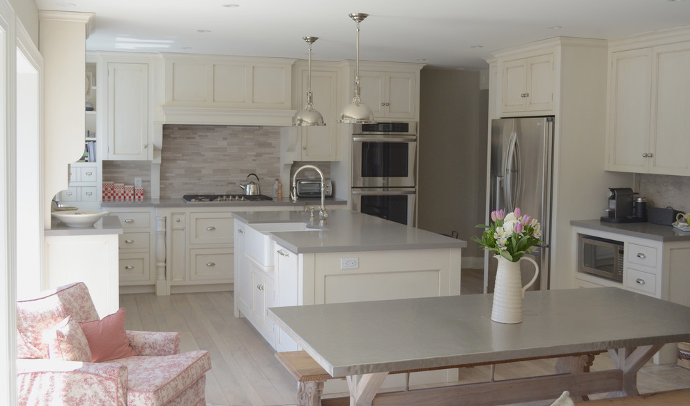 Example of a mid-sized transitional l-shaped light wood floor eat-in kitchen design in Toronto with a farmhouse sink, white cabinets, quartz countertops, gray backsplash, stone tile backsplash, stainless steel appliances, an island and shaker cabinets