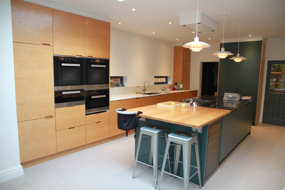 ロンドンにある広いコンテンポラリースタイルのおしゃれなキッチン (フラットパネル扉のキャビネット、淡色木目調キャビネット、シルバーの調理設備、アンダーカウンターシンク、木材カウンター、グレーの床、茶色いキッチンカウンター) の写真