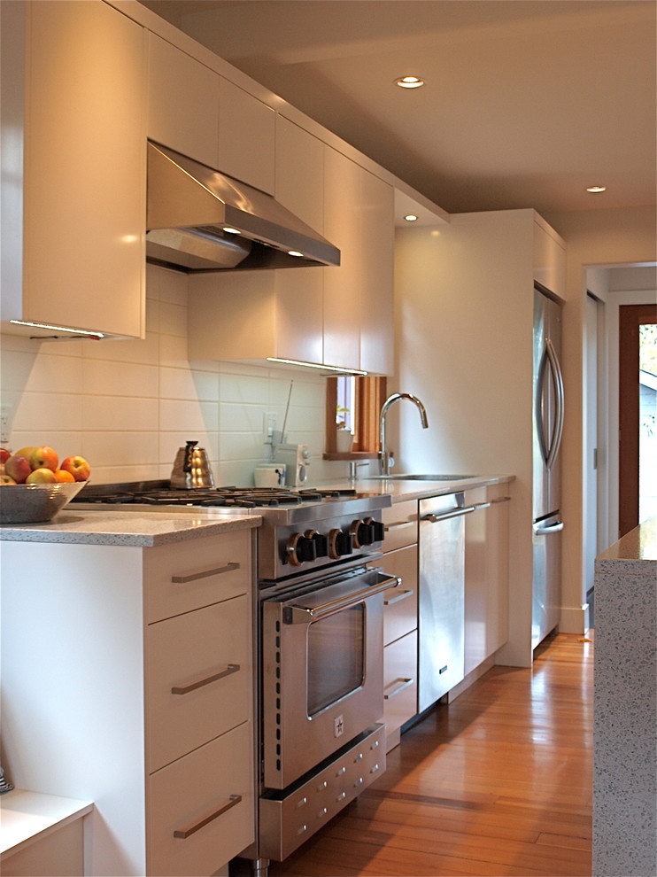 Bild på ett funkis linjärt kök och matrum, med en undermonterad diskho, släta luckor, vita skåp, bänkskiva i kvarts, vitt stänkskydd, stänkskydd i glaskakel och rostfria vitvaror