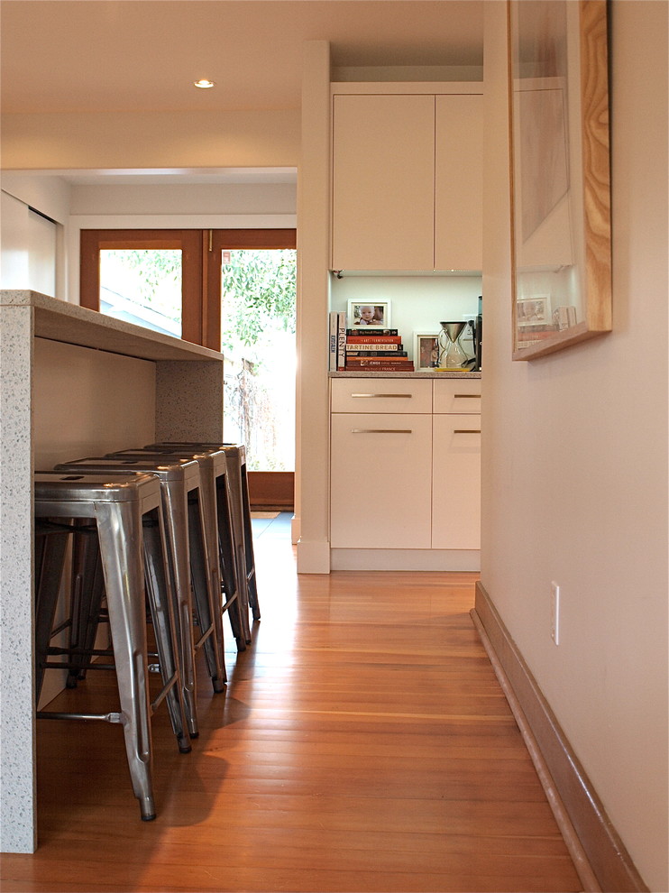 Foto på ett funkis linjärt kök och matrum, med en undermonterad diskho, släta luckor, vita skåp, bänkskiva i kvarts, vitt stänkskydd, stänkskydd i glaskakel och rostfria vitvaror