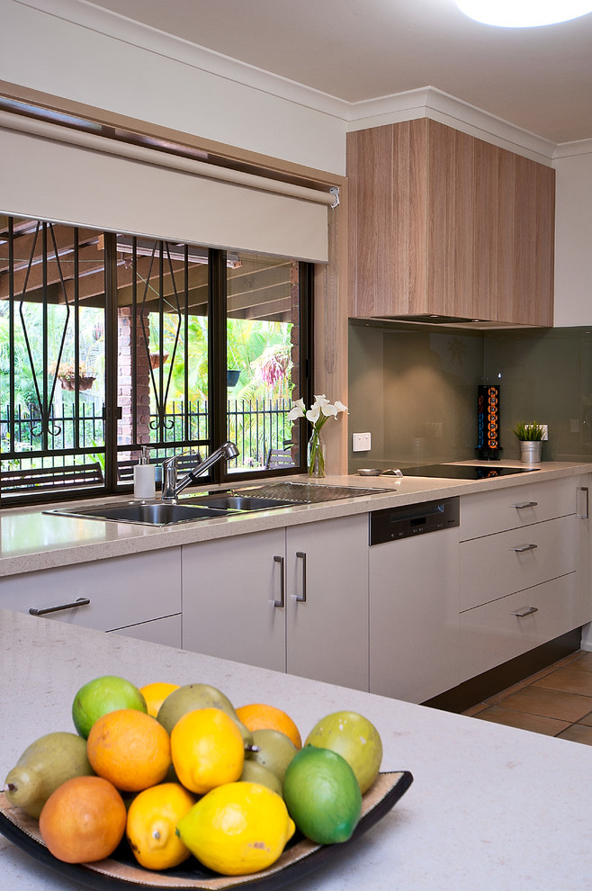Medium sized modern l-shaped kitchen in Brisbane with a built-in sink, flat-panel cabinets, beige cabinets, engineered stone countertops, green splashback, glass sheet splashback, integrated appliances, ceramic flooring and no island.