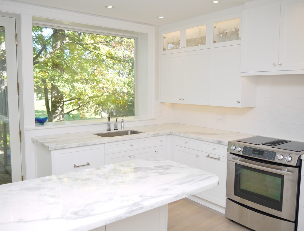 Example of a large classic u-shaped light wood floor eat-in kitchen design in Toronto with an undermount sink, recessed-panel cabinets, white cabinets, quartzite countertops, white backsplash, ceramic backsplash, stainless steel appliances and an island