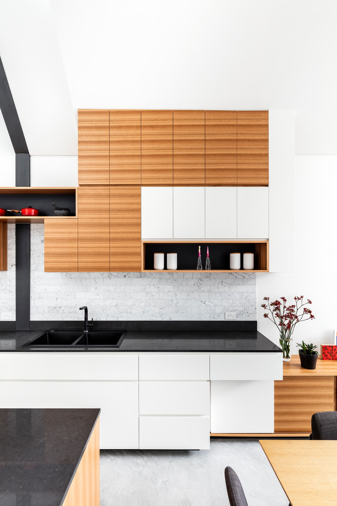 Bild på ett mellanstort funkis svart svart kök och matrum, med en dubbel diskho, släta luckor, vita skåp, bänkskiva i kvarts, grått stänkskydd, rostfria vitvaror, betonggolv, en köksö och grått golv
