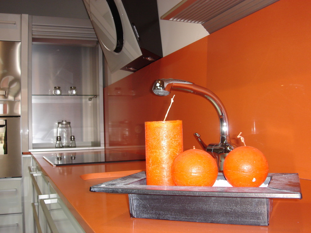 Modelo de cocinas en L actual de tamaño medio abierta con fregadero bajoencimera, puertas de armario blancas, encimera de cuarzo compacto, salpicadero naranja, electrodomésticos de acero inoxidable y suelo de madera clara