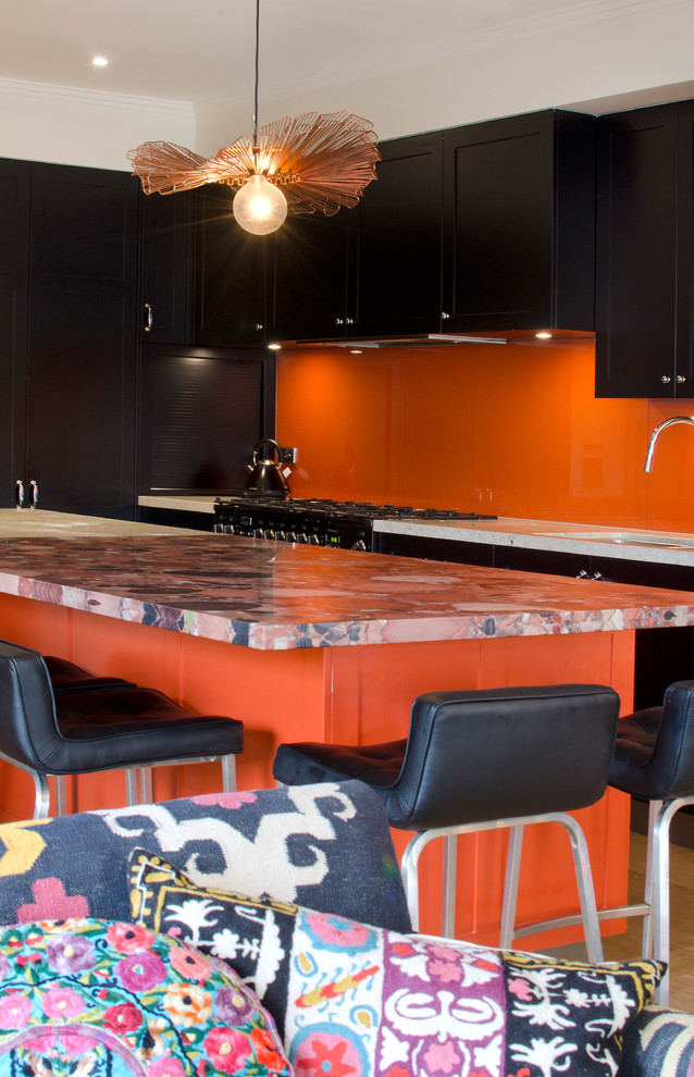 Große Eklektische Wohnküche in L-Form mit Unterbauwaschbecken, Schrankfronten im Shaker-Stil, schwarzen Schränken, Granit-Arbeitsplatte, Küchenrückwand in Orange, Glasrückwand, Küchengeräten aus Edelstahl, braunem Holzboden und Kücheninsel in Melbourne