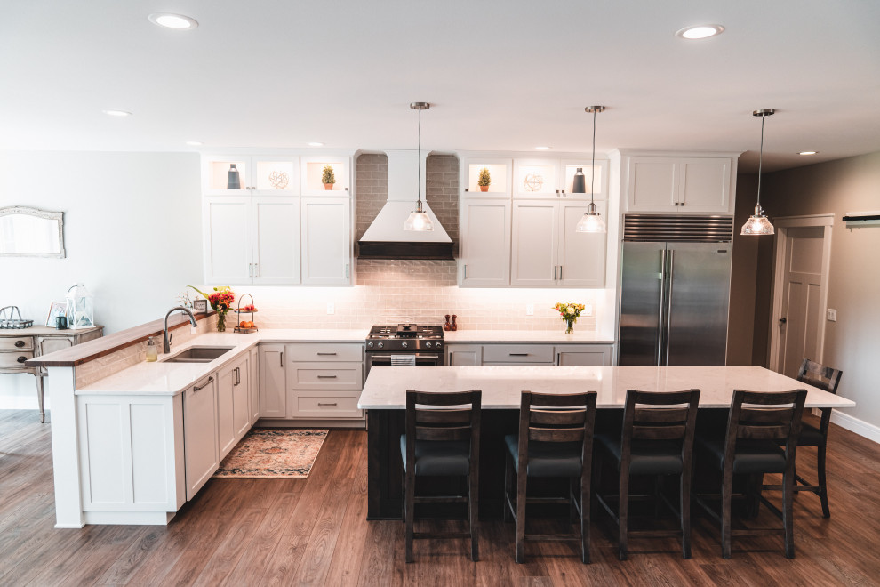 Example of a large transitional l-shaped vinyl floor and brown floor kitchen pantry design in Other with an undermount sink, shaker cabinets, white cabinets, quartz countertops, gray backsplash, subway tile backsplash, stainless steel appliances, an island and white countertops