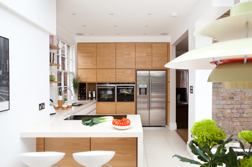 Mittelgroße Moderne Wohnküche in U-Form mit flächenbündigen Schrankfronten, hellen Holzschränken, Küchengeräten aus Edelstahl und Halbinsel in London