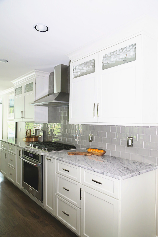 Example of a mid-sized transitional single-wall medium tone wood floor enclosed kitchen design in Other with an undermount sink, recessed-panel cabinets, white cabinets, marble countertops, gray backsplash, glass tile backsplash, stainless steel appliances and no island