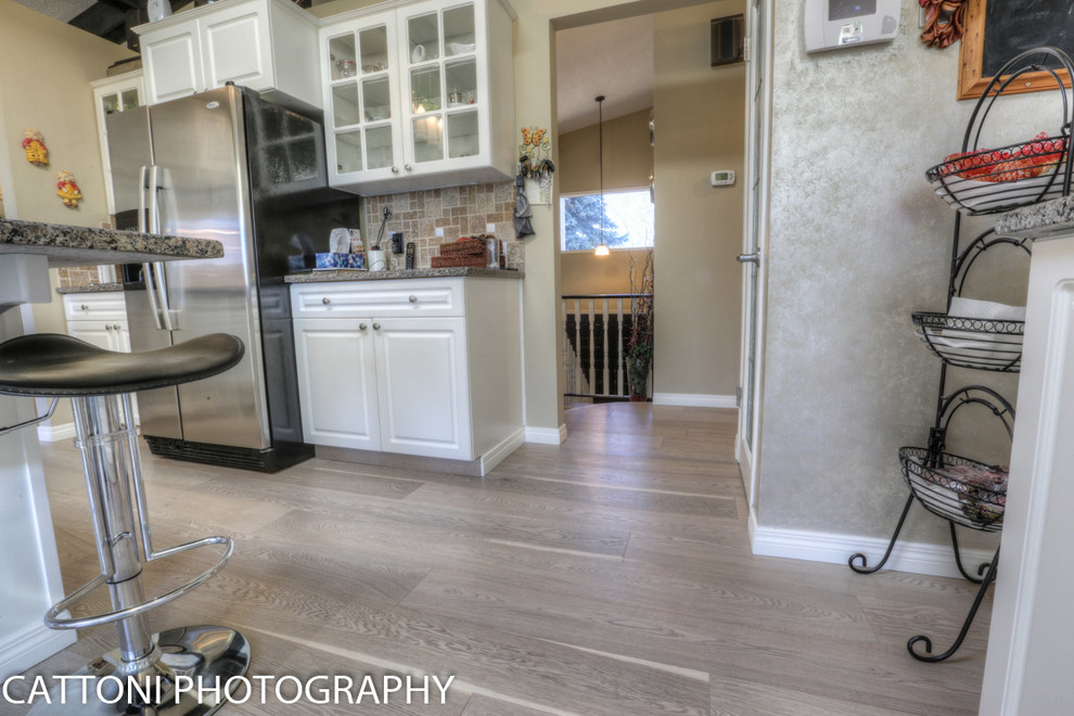Bild på ett avskilt, mellanstort funkis u-kök, med en dubbel diskho, granitbänkskiva, beige stänkskydd, stänkskydd i keramik, rostfria vitvaror, ljust trägolv, en köksö, luckor med glaspanel, vita skåp och grått golv