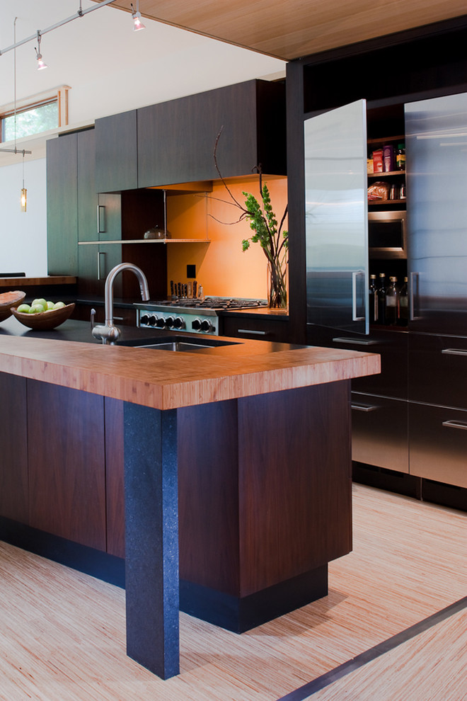 Modelo de cocina minimalista con armarios con paneles lisos, puertas de armario de madera en tonos medios y electrodomésticos de acero inoxidable