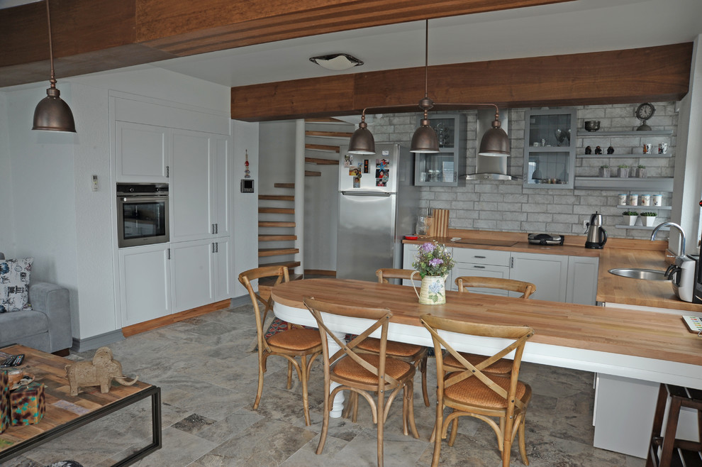 Maritim inredning av ett litet kök, med en enkel diskho, öppna hyllor, vita skåp, bänkskiva i zink, travertin golv och en köksö