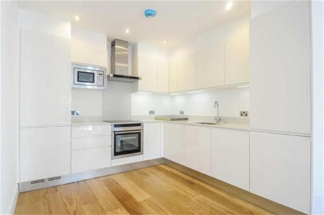 This is an example of a medium sized contemporary l-shaped open plan kitchen in London with a submerged sink, flat-panel cabinets, white cabinets, quartz worktops, white splashback, glass sheet splashback, stainless steel appliances, medium hardwood flooring and an island.
