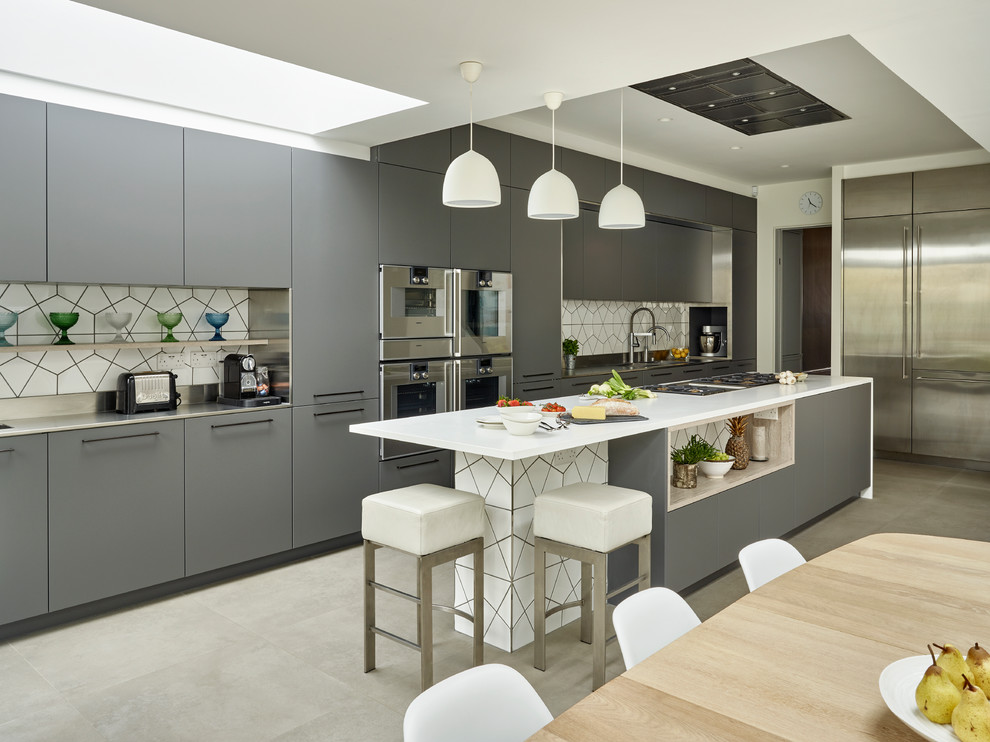Design ideas for a contemporary open plan kitchen in London with an integrated sink, flat-panel cabinets, grey cabinets, composite countertops, white splashback, ceramic splashback, stainless steel appliances, ceramic flooring, an island and grey floors.