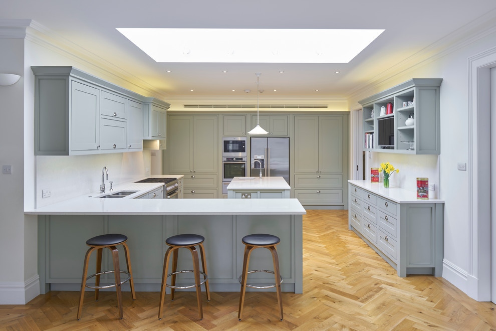 Design ideas for a large classic l-shaped open plan kitchen in London with a double-bowl sink, recessed-panel cabinets, grey cabinets, composite countertops, white splashback, stainless steel appliances, medium hardwood flooring and multiple islands.