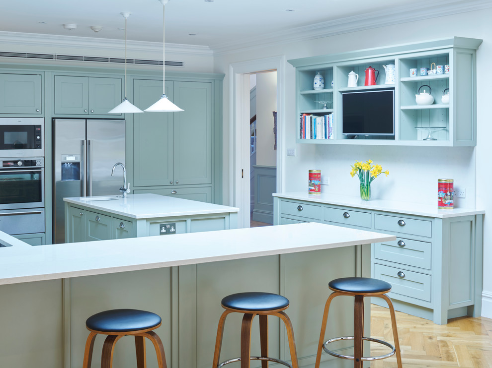Photo of a large traditional l-shaped open plan kitchen in London with a double-bowl sink, recessed-panel cabinets, grey cabinets, composite countertops, white splashback, stainless steel appliances, medium hardwood flooring and multiple islands.