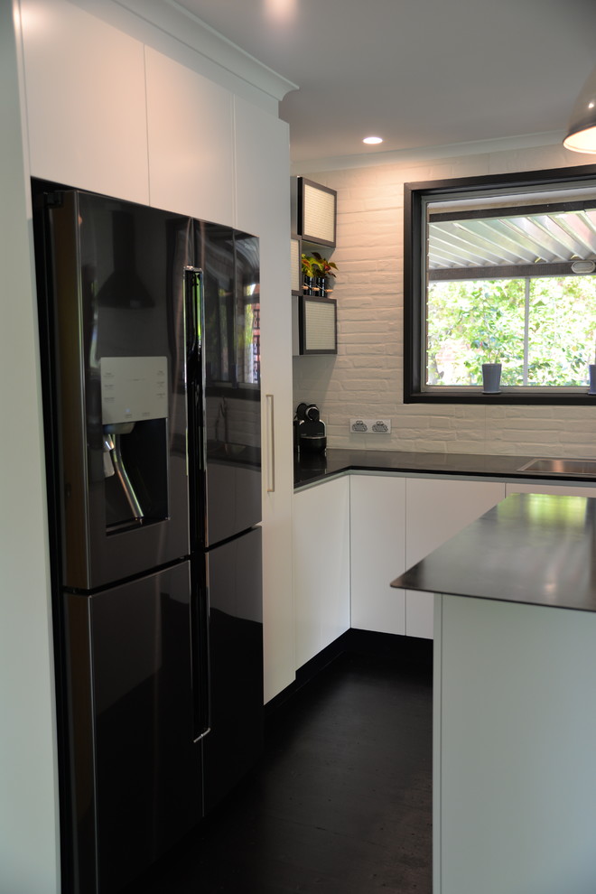 Design ideas for a medium sized industrial l-shaped kitchen/diner in Canberra - Queanbeyan with a built-in sink, flat-panel cabinets, white cabinets, stainless steel worktops, white splashback, ceramic splashback, black appliances, painted wood flooring and an island.