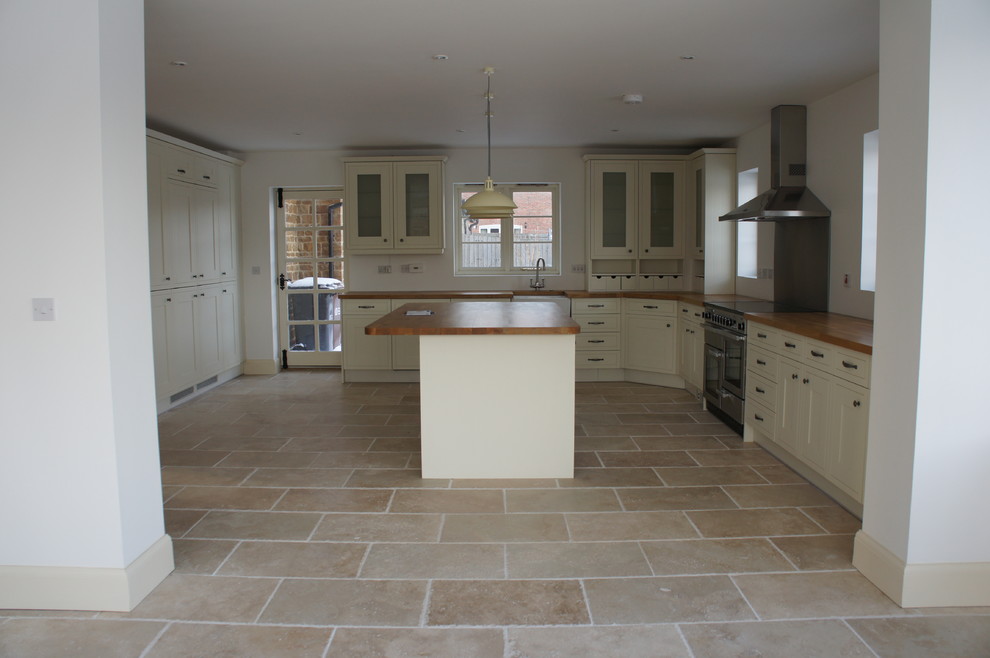 This is an example of a large farmhouse kitchen/diner in Other with a belfast sink, shaker cabinets, white cabinets, wood worktops, travertine flooring and an island.