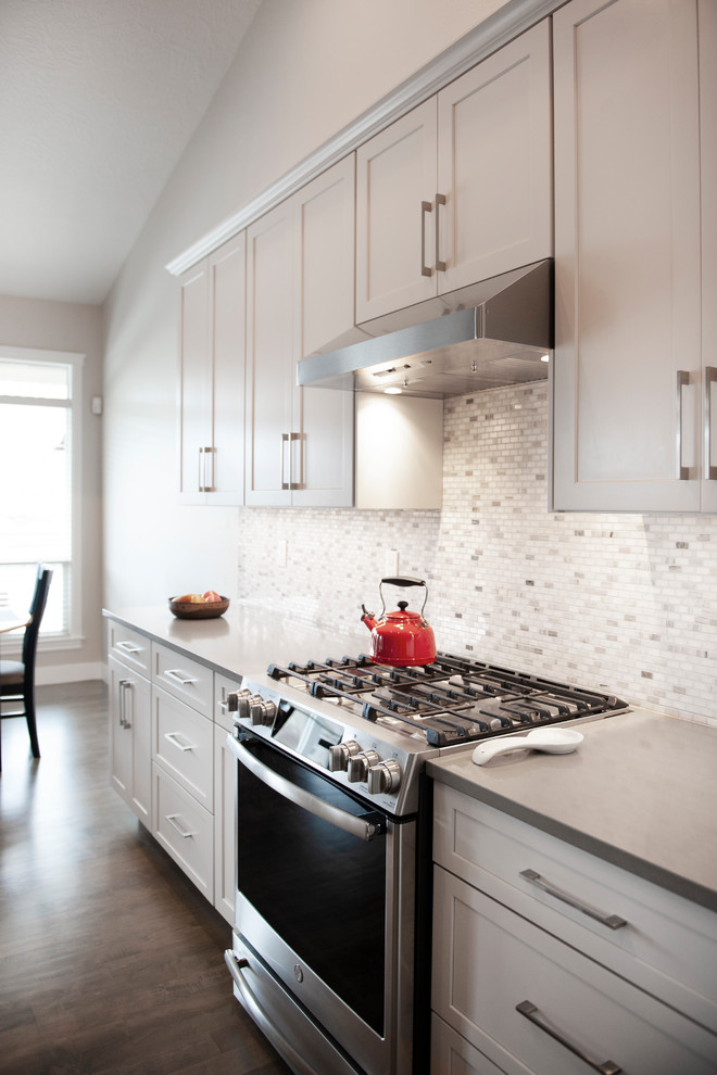 Idéer för att renovera ett mellanstort funkis grå grått kök, med en undermonterad diskho, skåp i shakerstil, vita skåp, laminatbänkskiva, vitt stänkskydd, stänkskydd i keramik, rostfria vitvaror, mellanmörkt trägolv, en köksö och brunt golv